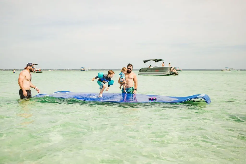 A family playing on a floating mat in the water off a pontoon boat