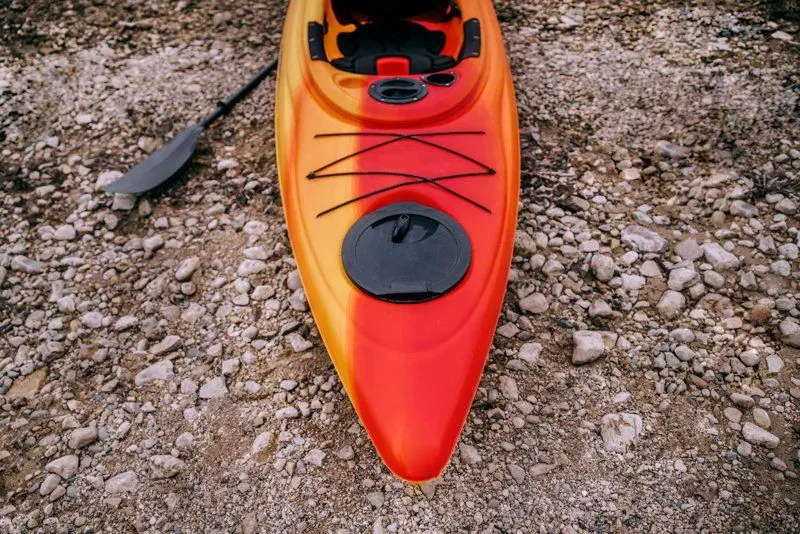 A red and orange single kayak resting on the shore
