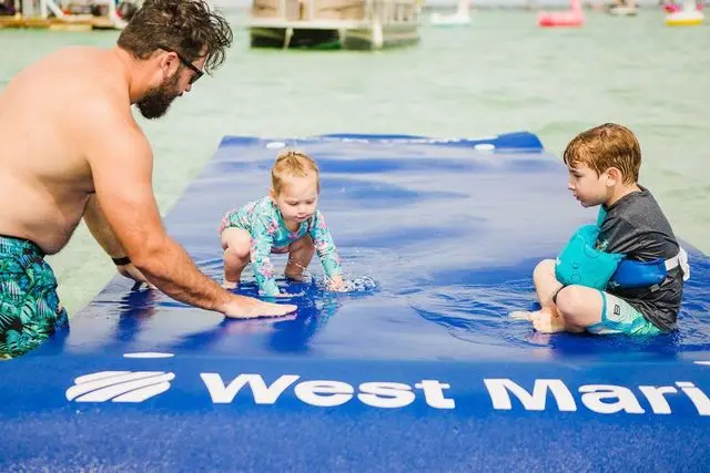 Kids playing on a floating mat behind a pontoon boat